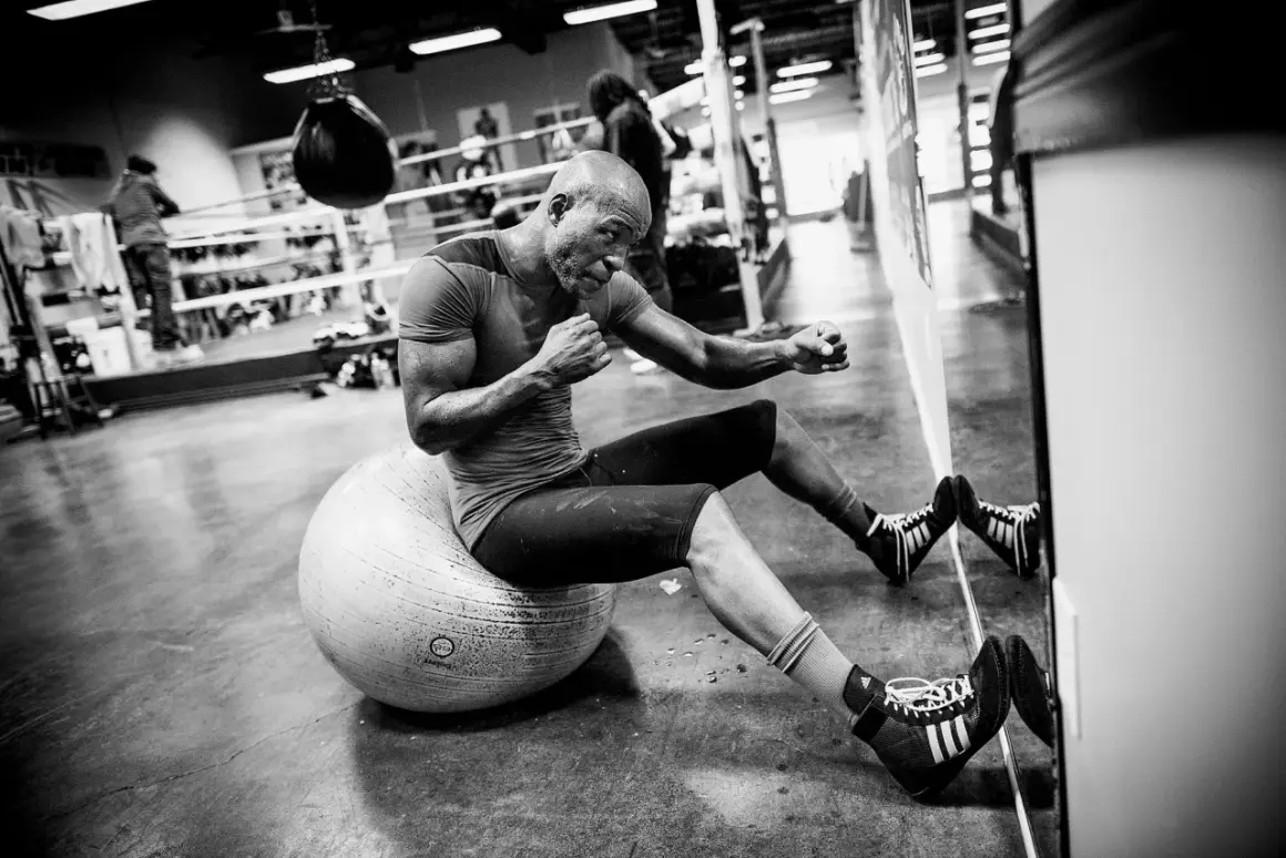 A determined Hopkins boxer, sweat glistening, trains on a stability ball in a boxing gym.