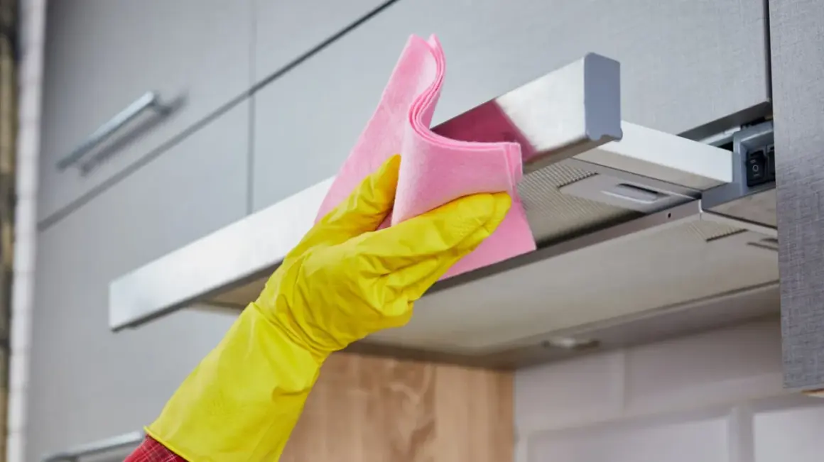 Gelbe Handschuhe und ein rosa Tuch reinigen die klebrige Dunstabzugshaube.