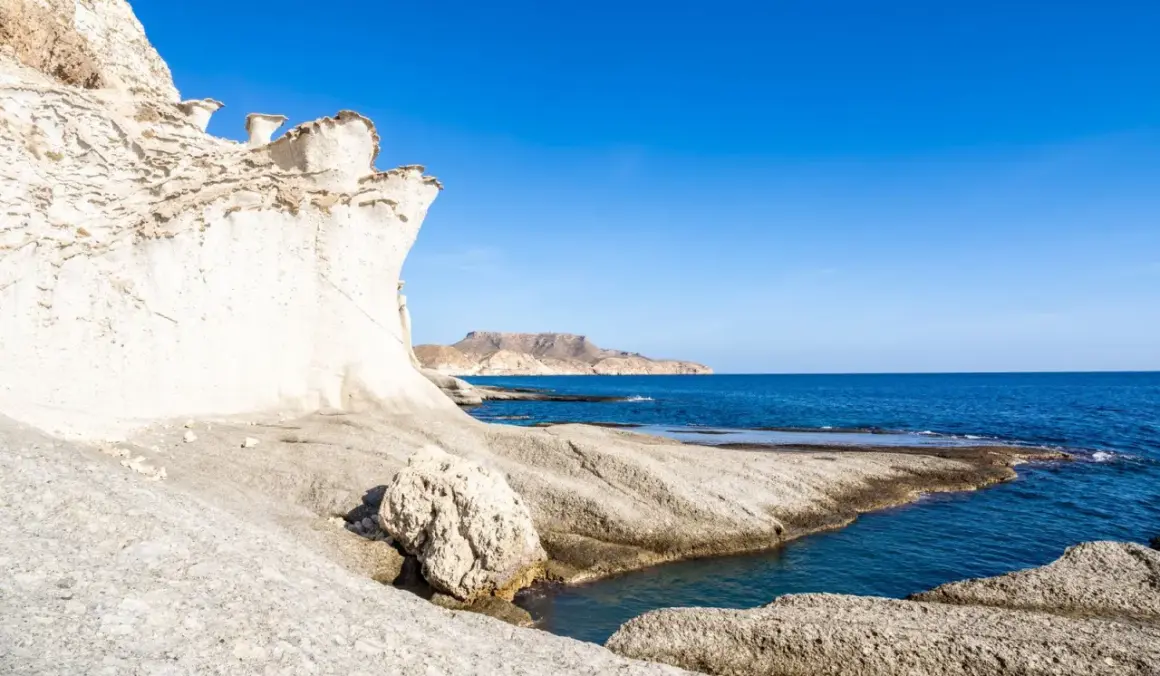 Formaciones rocosas blancas y erosionadas en una cala blanca Almería, con el mar azul intenso y montañas al fondo.
