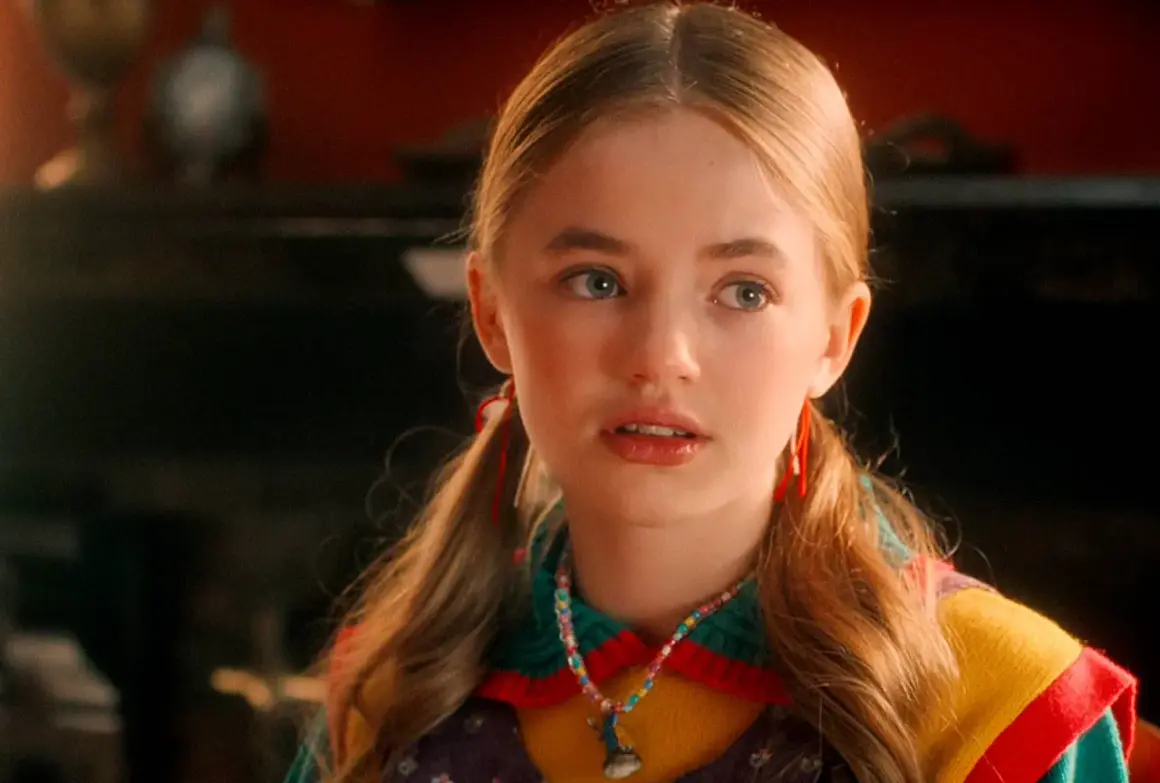 Holly Wheeler aus Stranger Things mit Zöpfen und einer bunten Halskette.