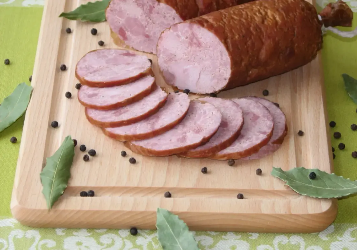 Kiełbasa szynkowa wędzona, pokrojona w plastry, na desce z pieprzem i liśćmi laurowymi. Idealna do domowego przepisu.