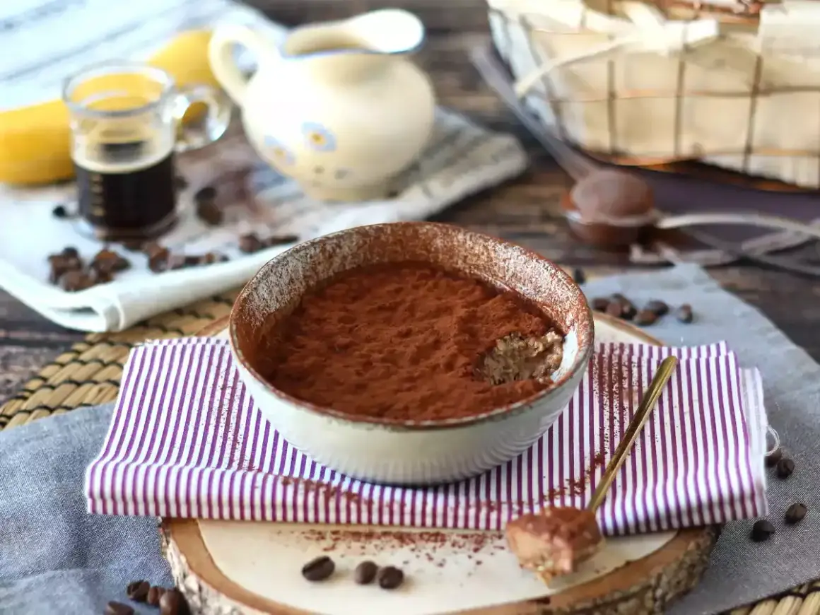 Schüssel mit Tiramisu Overnight Oats, bestäubt mit Kakao. Ein Löffel mit dem Dessert liegt daneben.