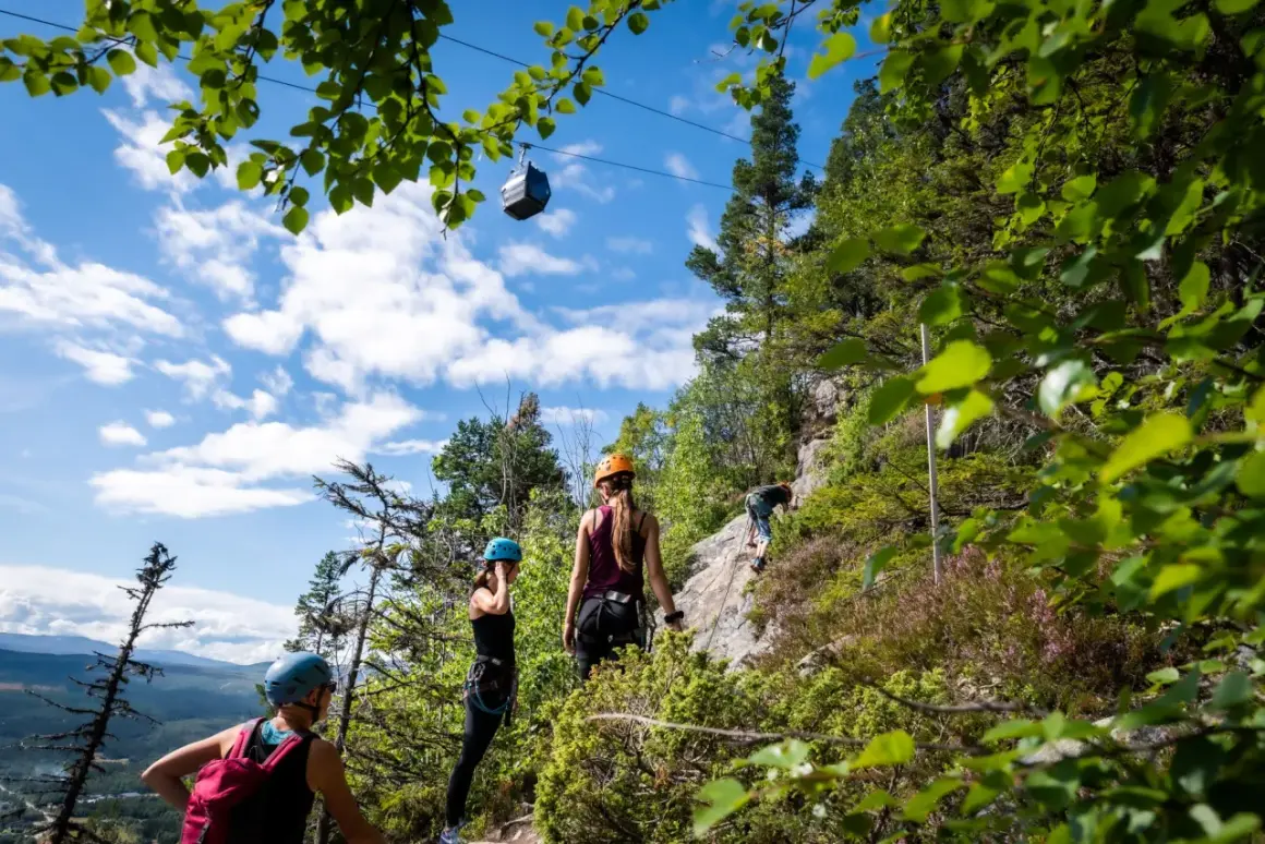 Äventyr vid Ramundberget: klättrare på klippvägg, linbana i skyn, vacker utsikt.