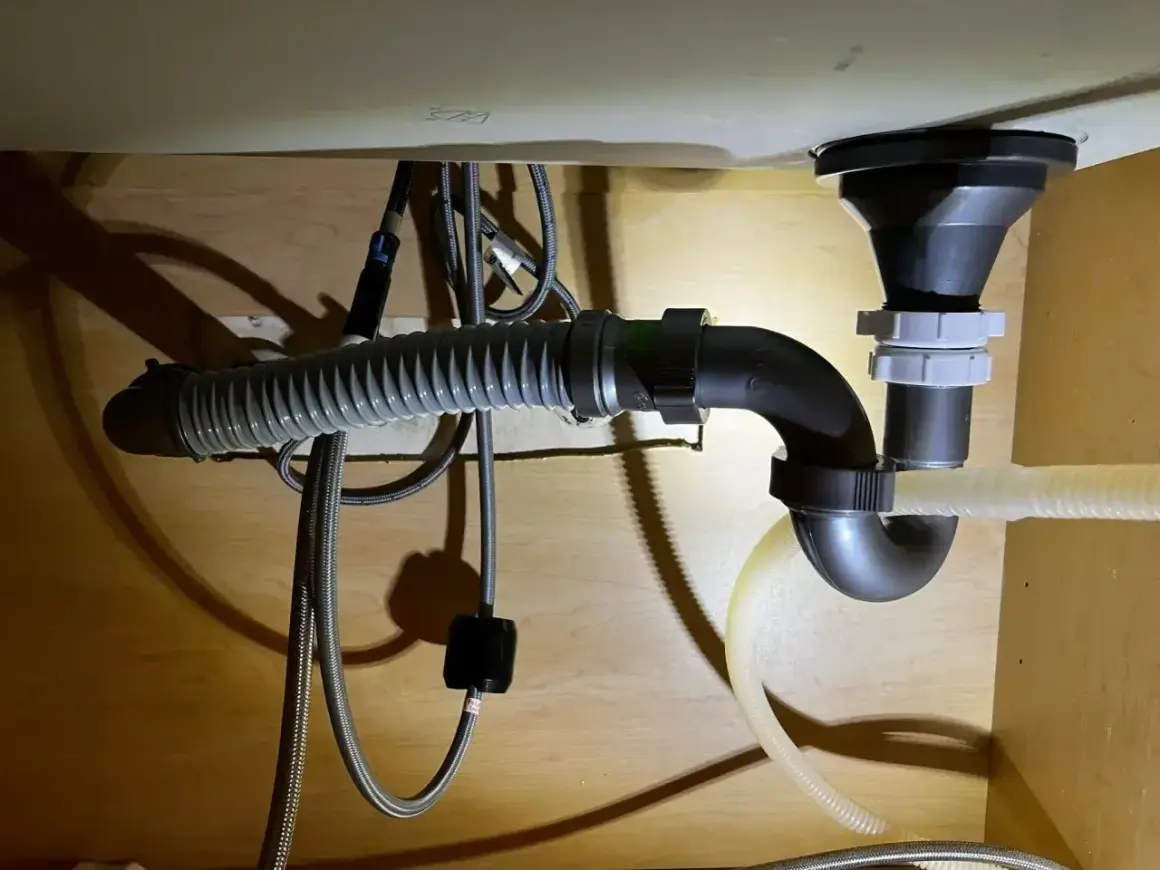 Pod zlewem widać instalację hydrauliczną z syfonem i elastycznym wężem odpływowym. Widać też trójnik, który rozdziela odpływ.