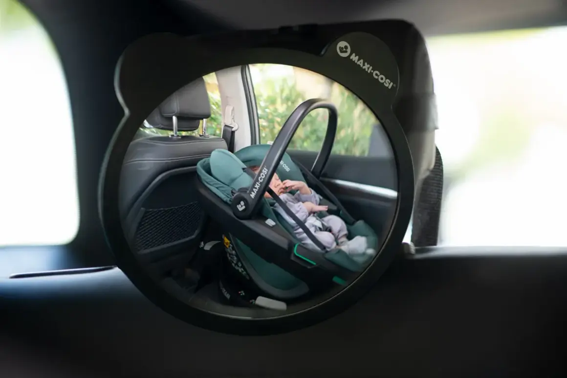 Ein Baby schläft friedlich in einer grünen Maxi-Cosi Babyschale im Rückspiegel eines Taxis.