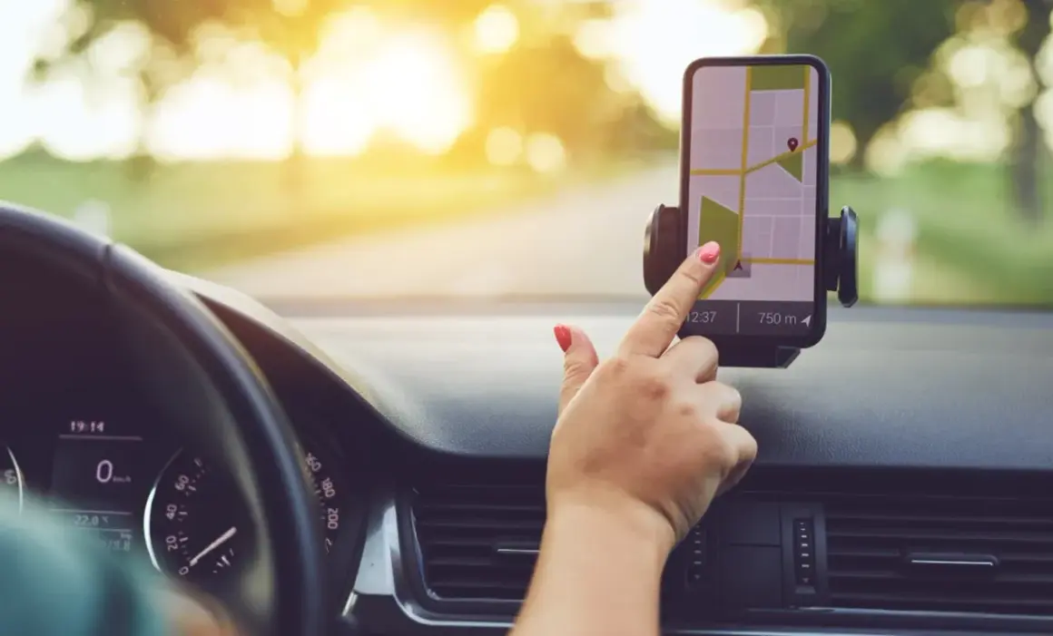 Dłoń z czerwonym lakierem na paznokciach dotyka ekranu telefonu z mapą, korzystając z nawigacji na telefon podczas jazdy.