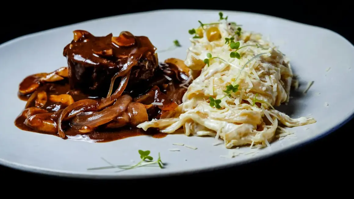 Gulasz angielski z wołowiny w sosie grzybowym, podany z kremowym makaronem tagliatelle posypanym parmezanem i kiełkami.