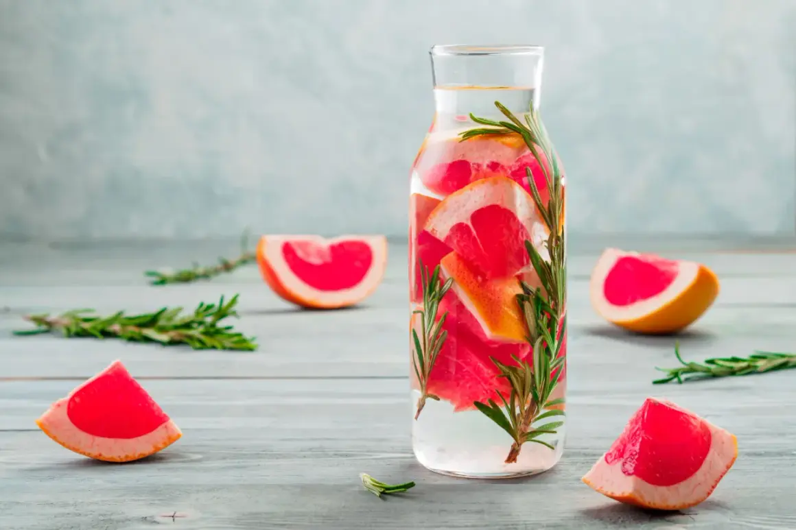 Erfrischendes Detox Wasser mit Grapefruit und Rosmarin in einer Glasflasche, umgeben von frischen Fruchtscheiben und Kräuterzweigen.