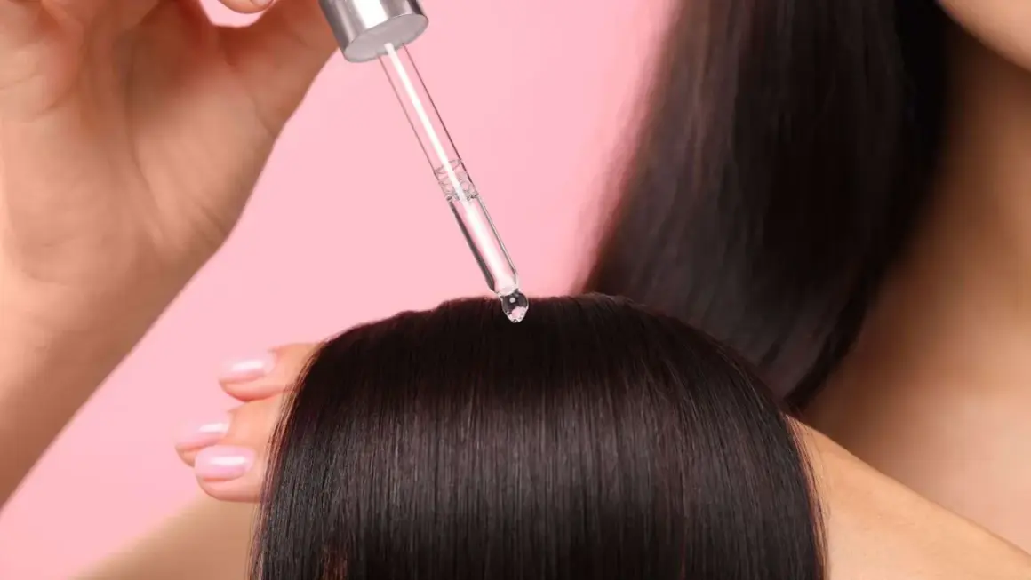 Une goutte de sérum tombe sur des cheveux bruns. Aide à choisir quel sérum choisir pour des cheveux brillants.