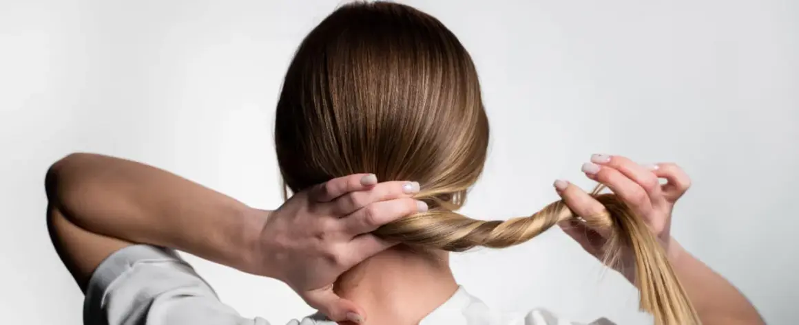 Manos trenzando el cabello rubio para crear peinados para dormir que mantengan el pelo bonito.