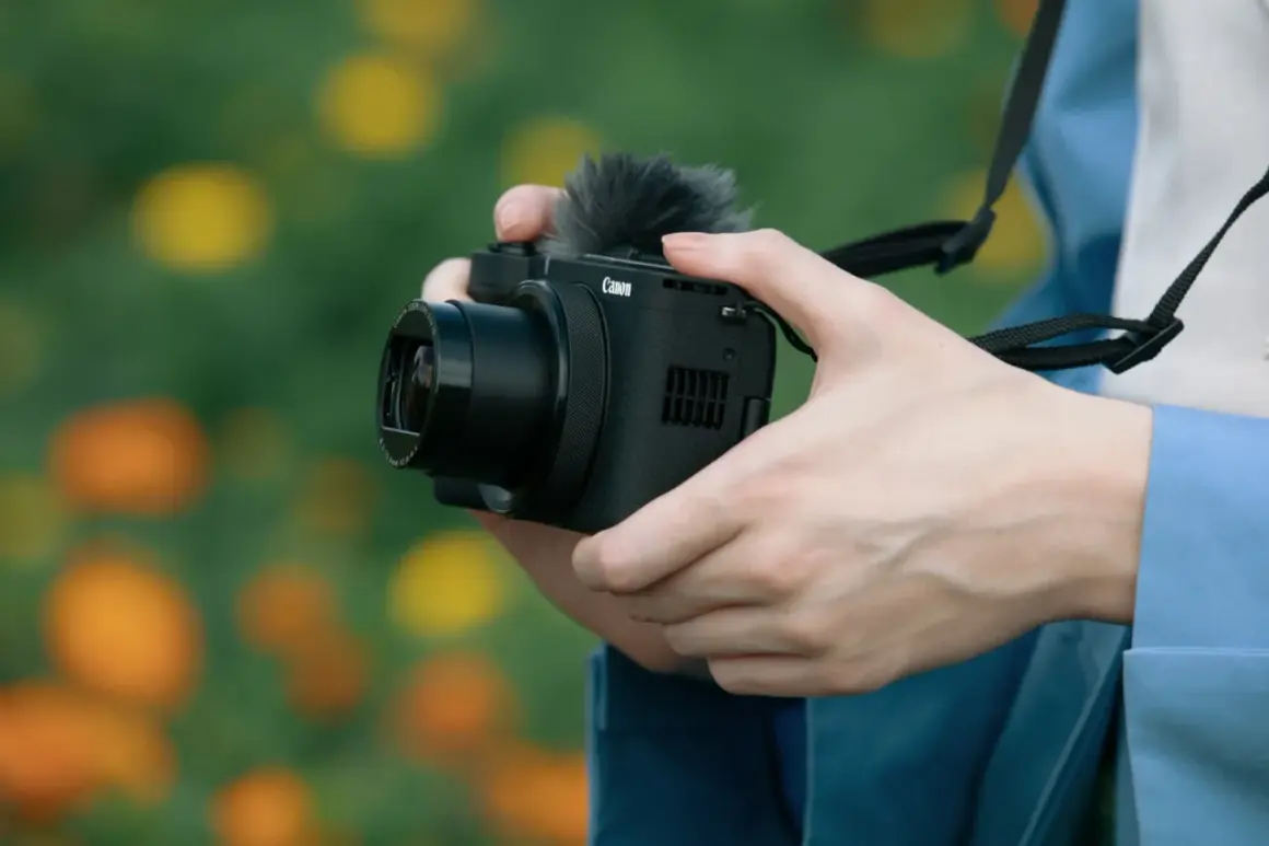 Dłonie trzymają aparat Canon z mikrofonem, gotowe do uchwycenia pięknych chwil. Aparat fotograficzny służy do tworzenia wspomnień.