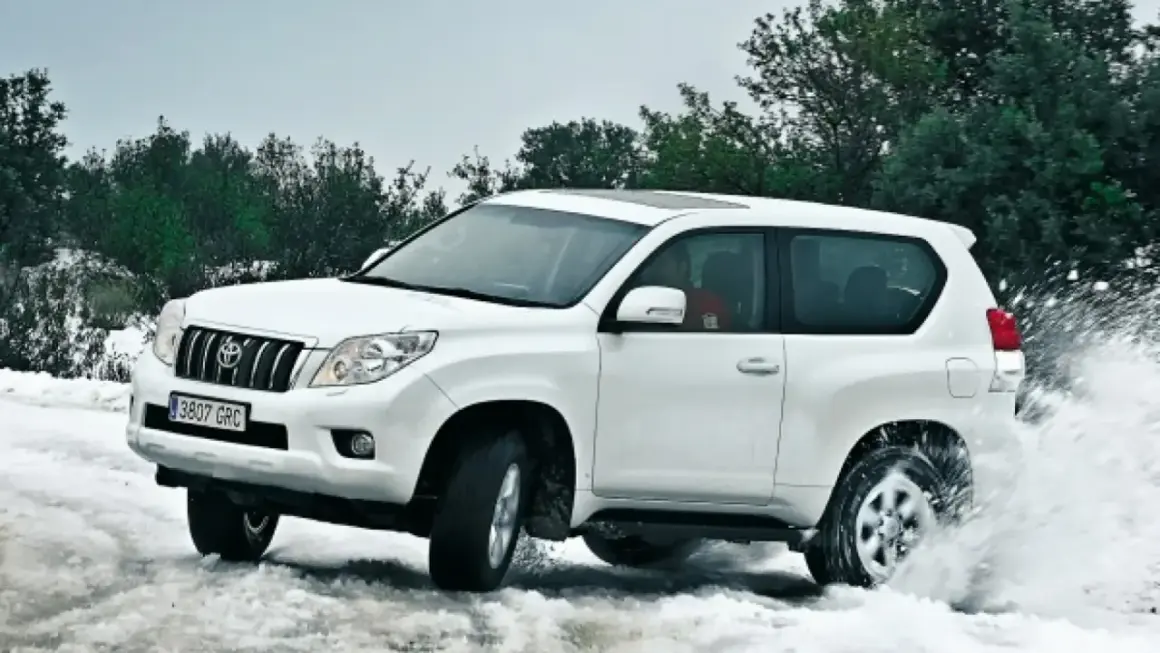 Toyota Land Cruiser 3.0 D4D 163 CV ficha técnica: un blanco todoterreno navega por nieve y agua, demostrando su potencia.
