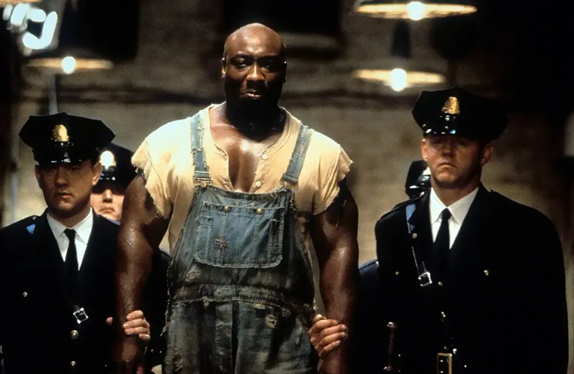John Coffey w ogrodniczkach, prowadzony przez strażników więziennych. Scena z filmu "Zielona mila 2".