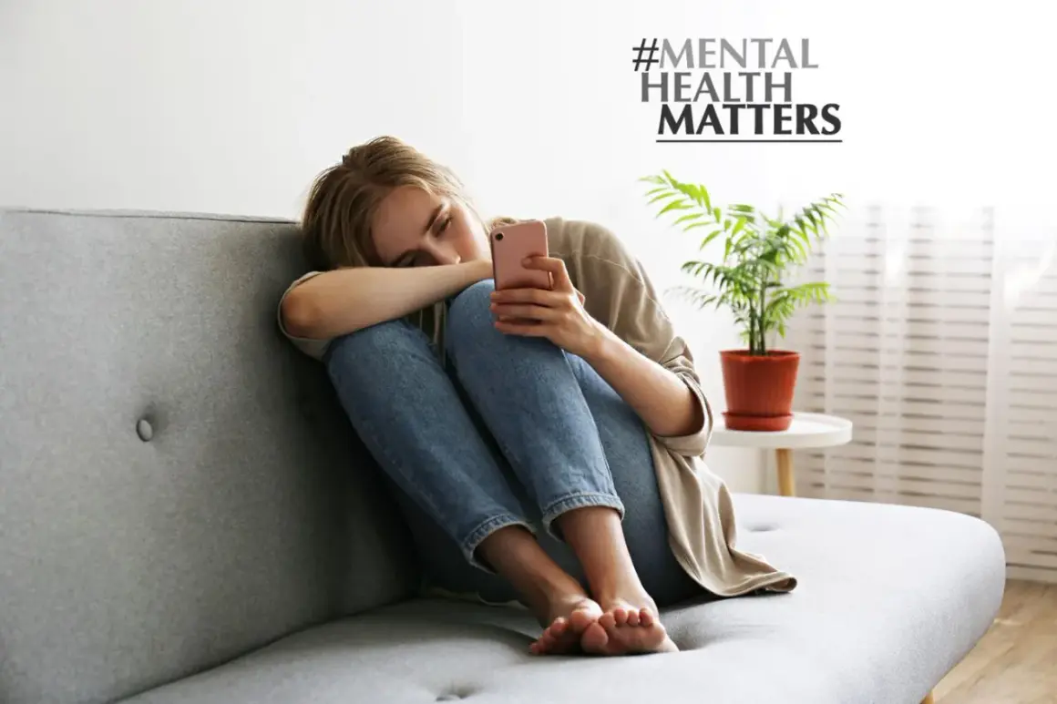 Junge Frau sitzt allein auf Sofa, depressiv weil single. Sie hält ihr Handy, #MENTAL HEALTH MATTERS.