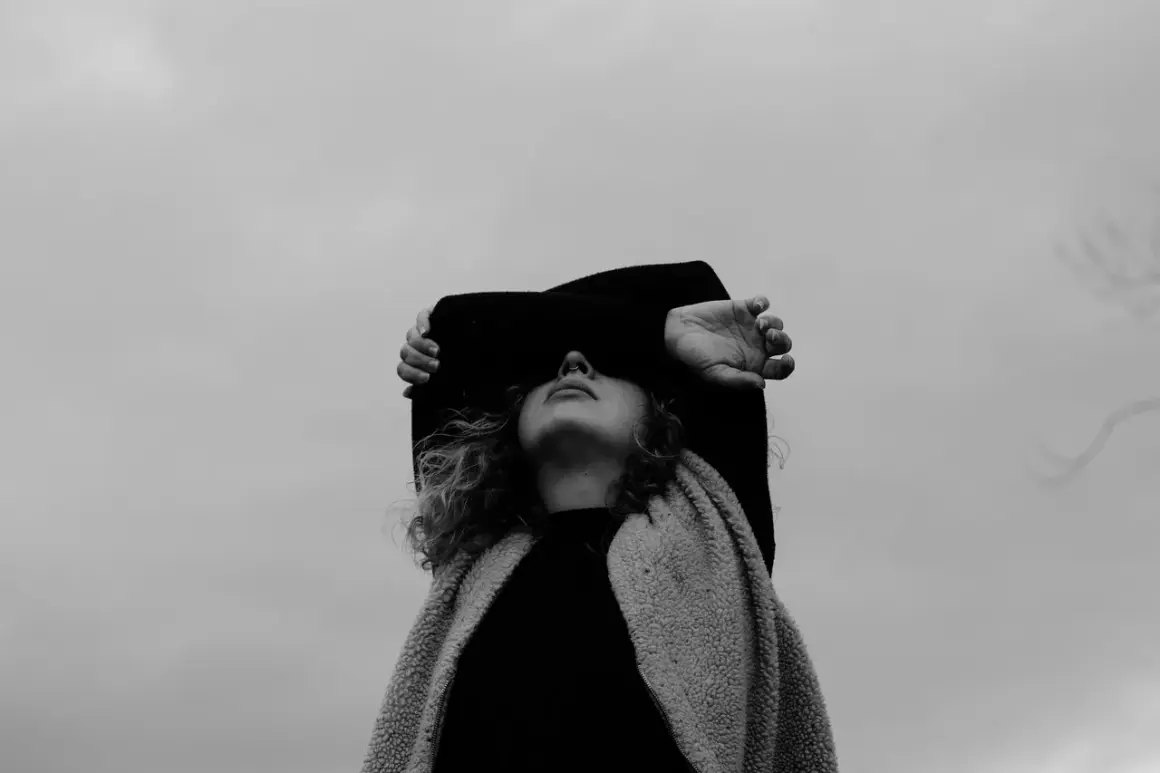 Osoba z zasłoniętymi oczami, czując ciężar depresji z objawami psychotycznymi, szuka ukojenia w szarym niebie.