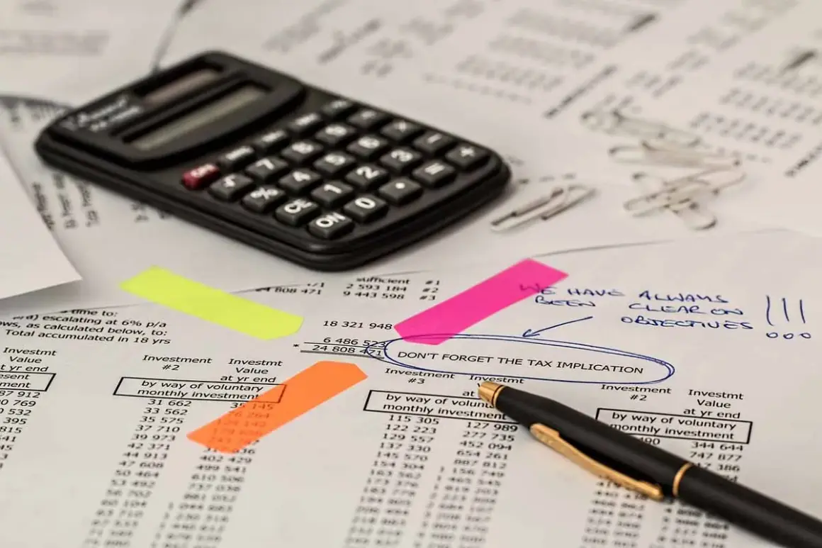 Kalkulator i dokumenty finansowe. Na jednym z nich zaznaczono "DON'T FORGET THE TAX IMPLICATION", co może dotyczyć np. podatek od gruntów rolnych poniżej 1 ha.