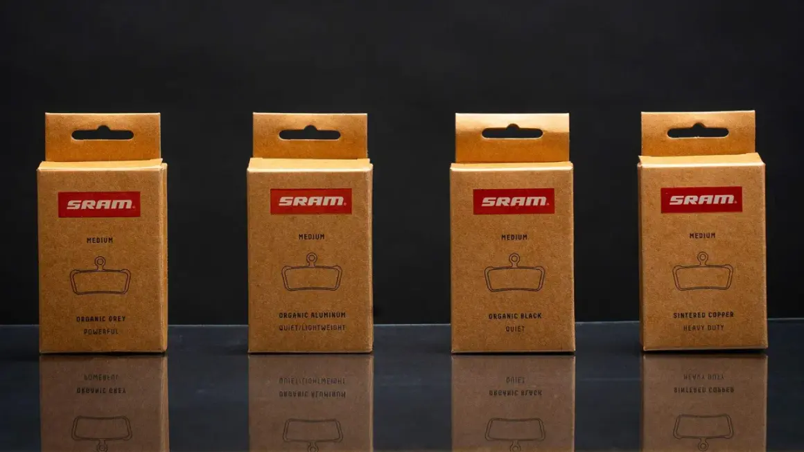 Cajas de SRAM mostrando distintos tipos de pastillas de freno: orgánicas (gris, aluminio, negra) y sinterizadas de cobre.