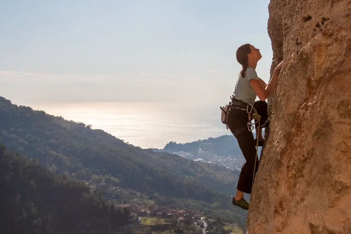Eine Frau klettert an einer Felswand in Finale Ligure. Im Hintergrund glitzert das Meer.