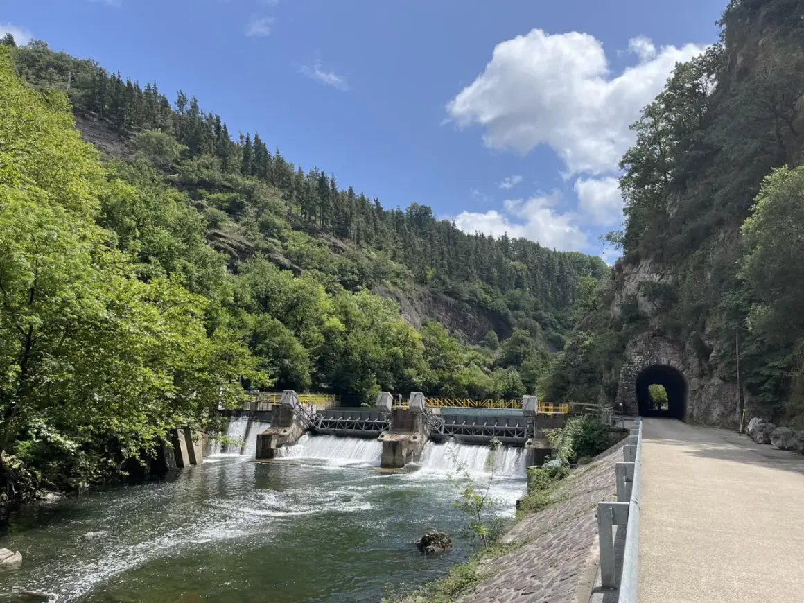 Un camino junto al río Bidasoa, con una presa y un túnel en la montaña.