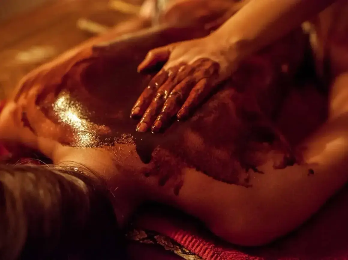Dłoń masuje plecy pokryte czekoladą do masażu spa. Ciemna, błyszcząca masa rozpływa się na skórze, tworząc relaksującą atmosferę.