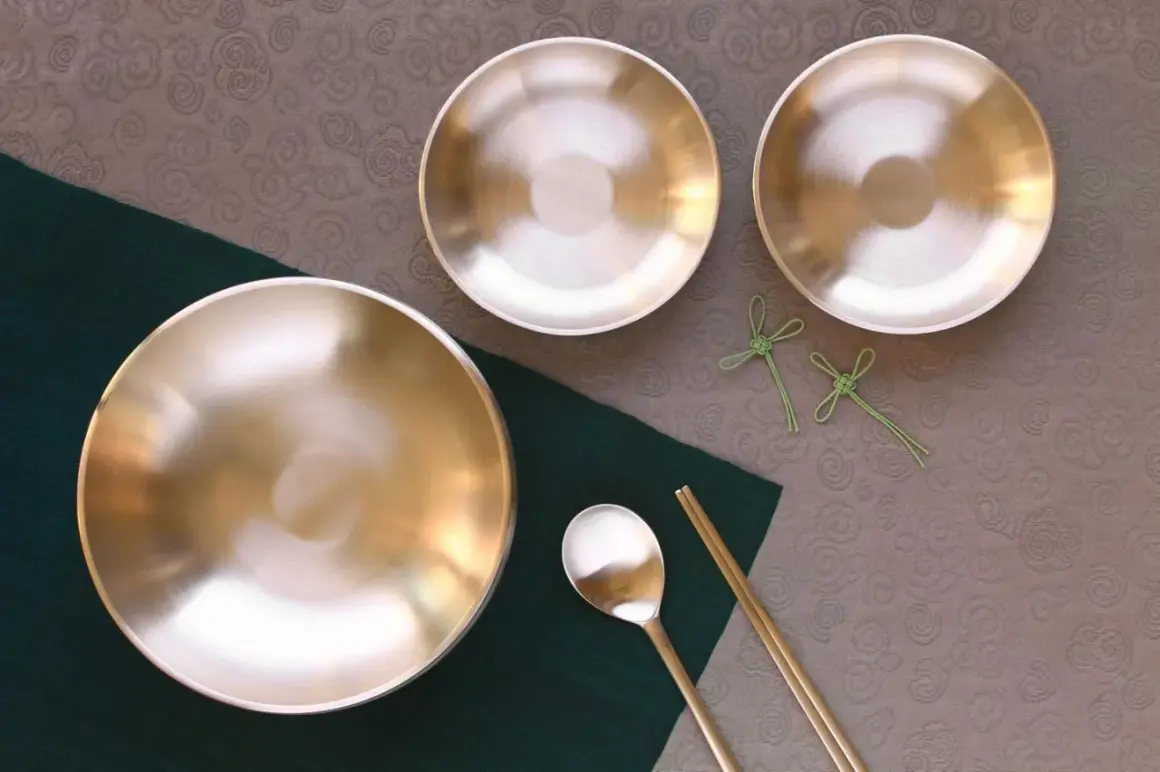 Glänzende Messingschalen, Löffel und Stäbchen auf einem Tisch. Perfekt für das Messing reinigen und eine elegante Mahlzeit.