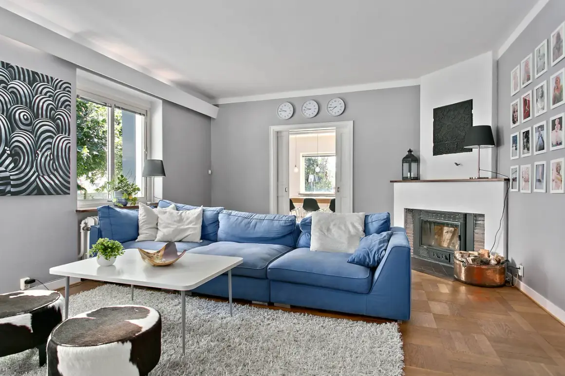 Blau passt toll zu seidengrau, wie dieses Wohnzimmer mit blauem Sofa, Kamin und Kuhfellhockern zeigt.