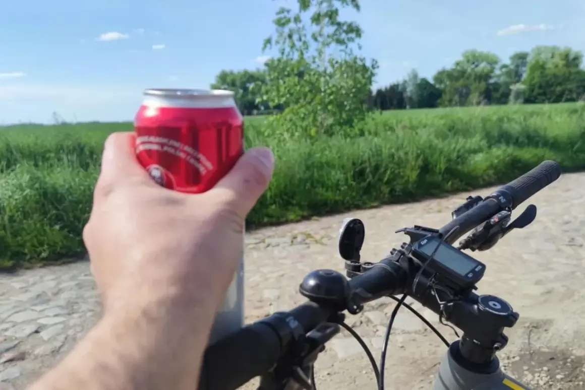 Rowerzysta trzyma puszkę napoju, planując jazdę rowerem po alkoholu. W tle zielone pola i błękitne niebo.