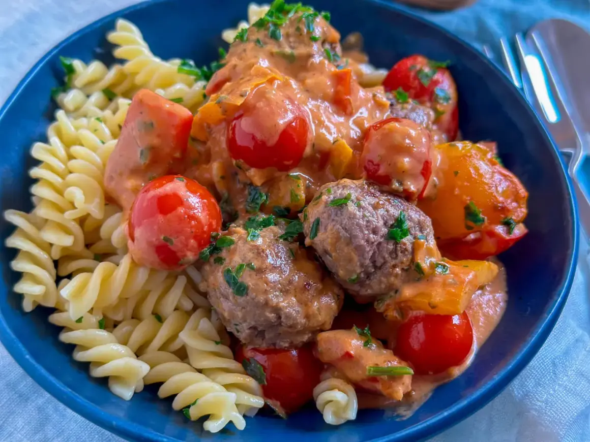 Herzhafte Hackfleisch Gerichte: saftige Hackbällchen in cremiger Tomatensoße mit Kirschtomaten und Fusilli-Nudeln, garniert mit frischer Petersilie.