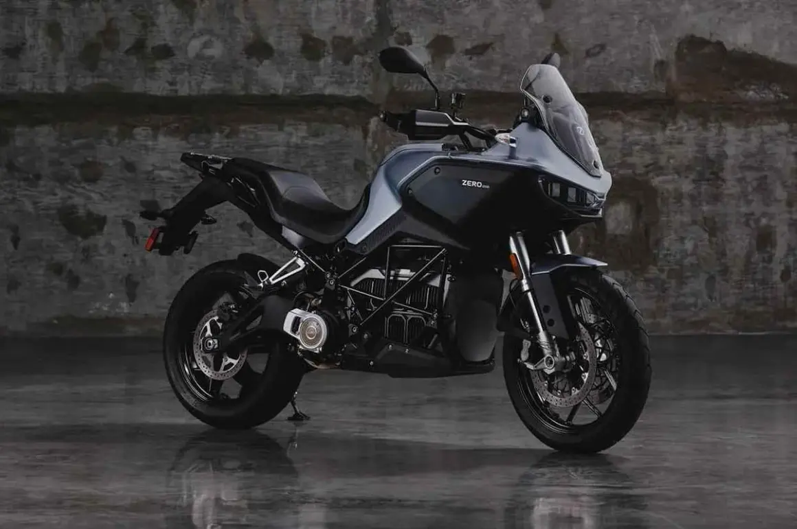 Motocicleta eléctrica Zero DSR/X, con potencia de 35kW, color gris oscuro, sobre suelo mojado y fondo de pared de ladrillo.