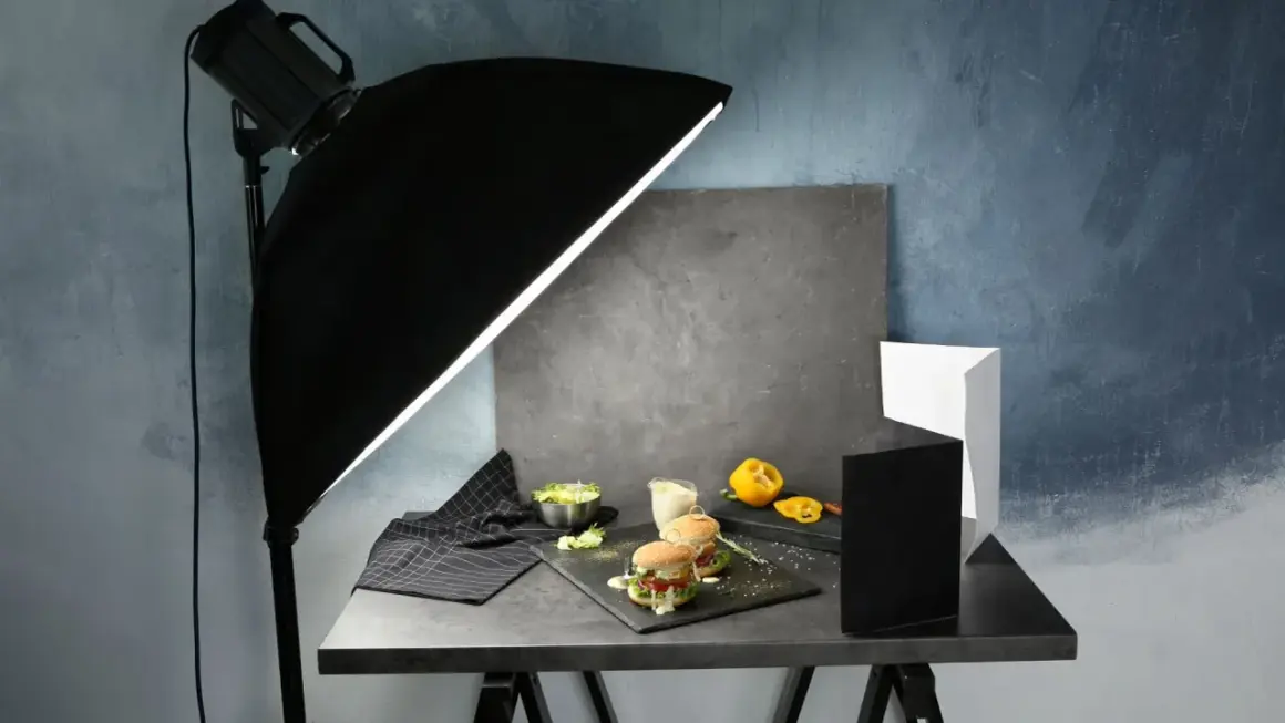 A food photography setup with burgers, salad, and a yellow pepper, illuminated by a large softbox, showcasing effective diy photography lighting.