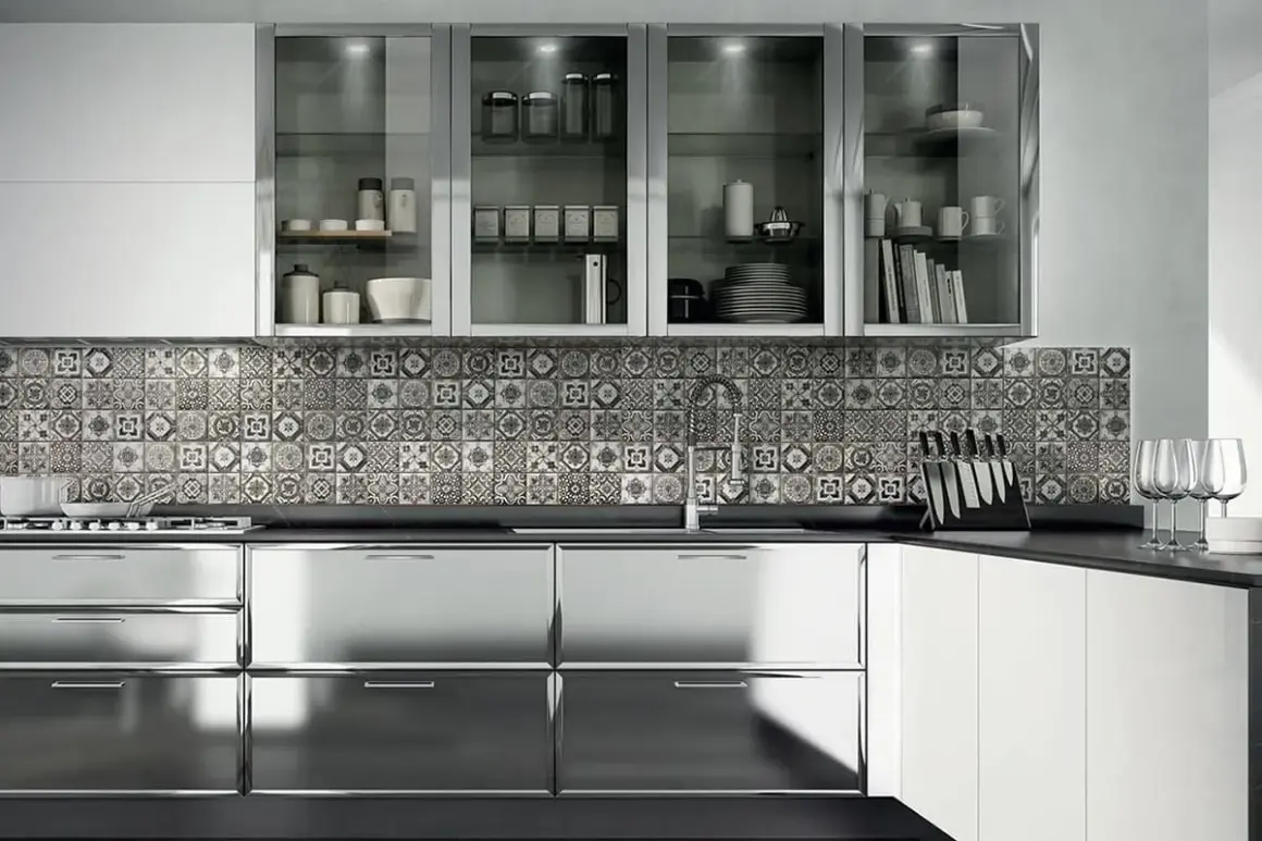 Cucina moderna con ante lucide in acciaio cromato o inox, piastrelle decorate e pensili in vetro.