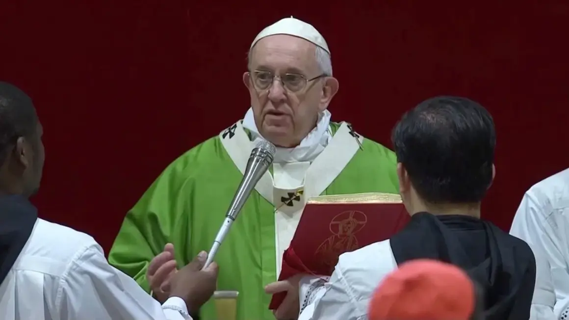 Papst Franziskus in grüner Messrobe hält eine Anrede. Vor ihm ein rotes Buch mit einem Bild.