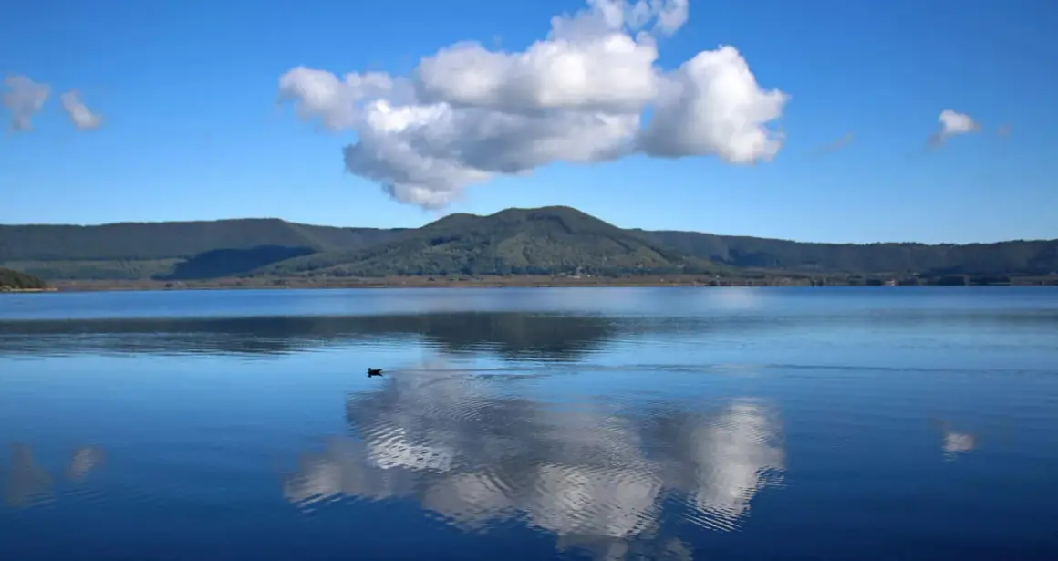 Un'oasi di pace al lago di Vici, con un cielo azzurro punteggiato da nuvole bianche che si specchiano sull'acqua calma.