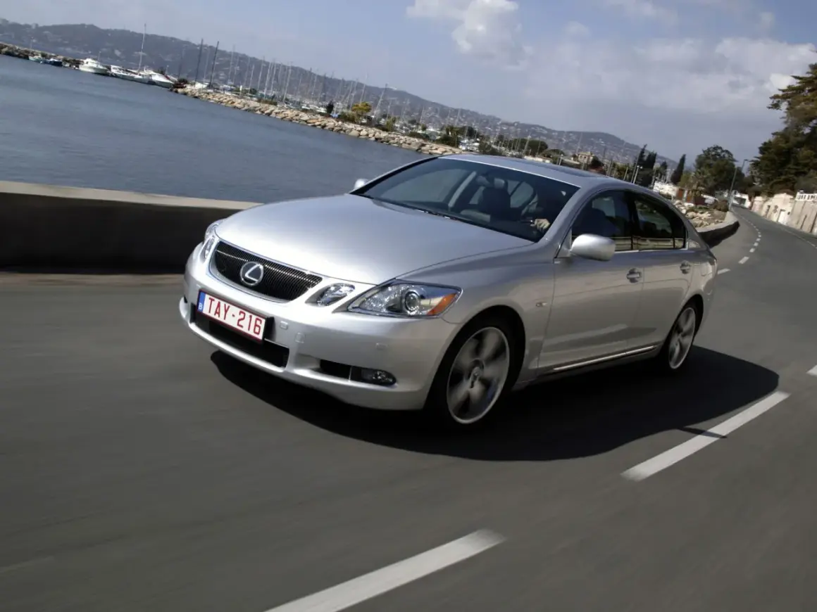 Srebrny Lexus GS300 MK3 pędzi wzdłuż malowniczego wybrzeża z widokiem na zatokę pełną jachtów.