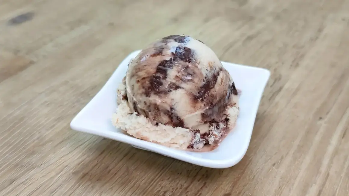 Ein Löffel cremiges Kinderriegel Eis mit Schokoladenstückchen auf einer weißen Schale.