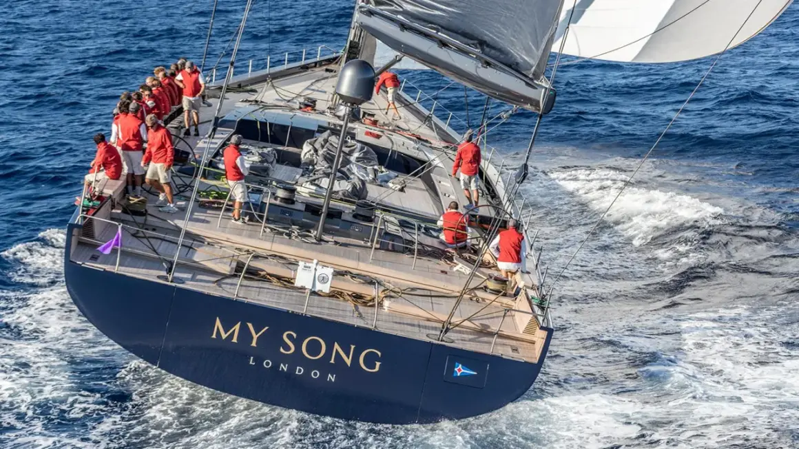 Equipaggio in rosso sul My Song yacht, che solca le onde blu. La vela nera e bianca cattura il vento.