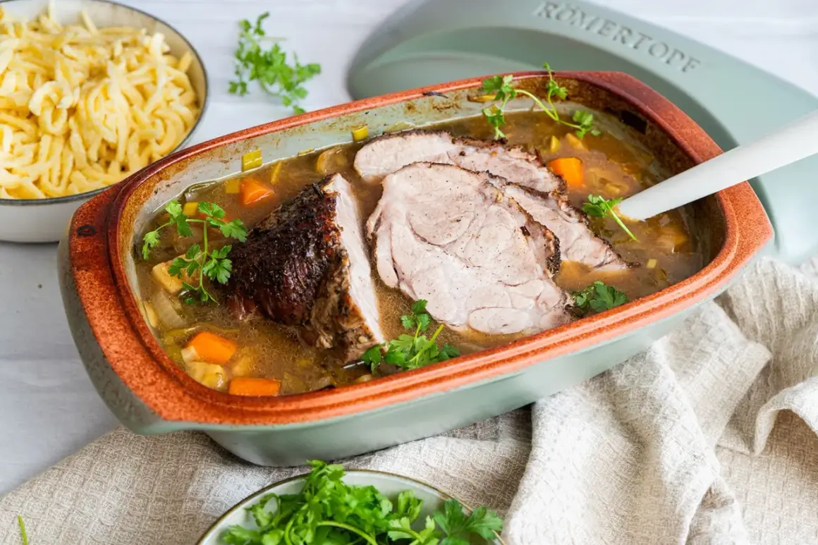 Saftiger schweinebraten im schmortopf, mit Karotten und Lauch, garniert mit Petersilie. Daneben eine Schüssel mit Spätzle.