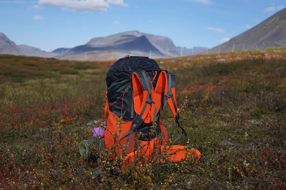 En stor ryggsäck står redo för mat utomhus i fjällterräng. En liggunderlag och en lila kudde syns vid sidan.