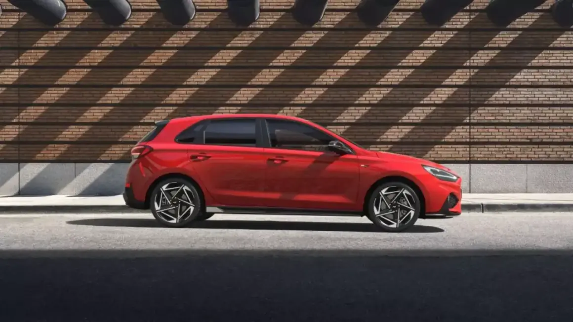 Czerwony Hyundai i30 hatchback stoi na tle ceglanej ściany z ciekawymi cieniami.
