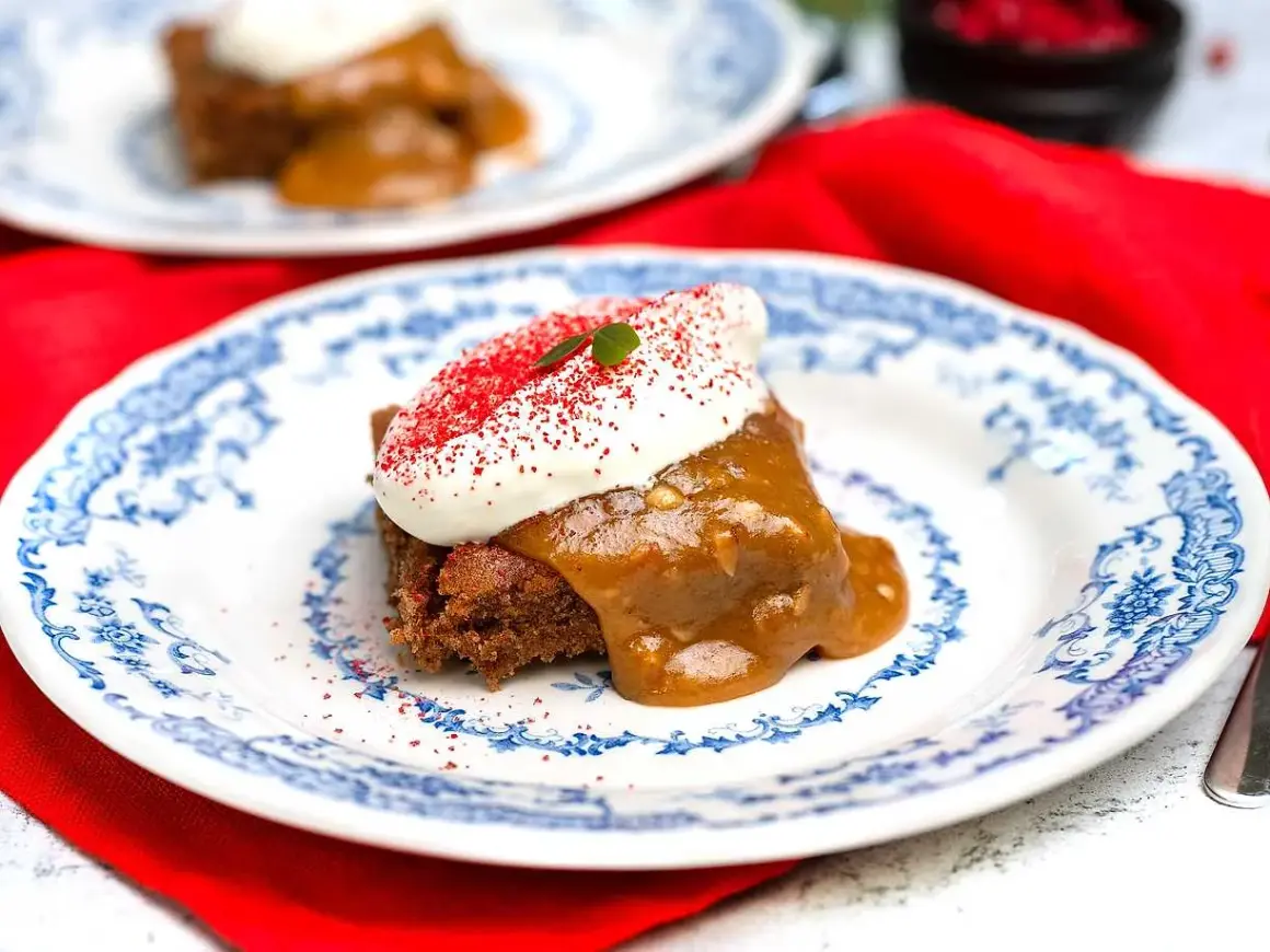 En bit saftig sockerkaka med pepparkakskrydda, toppad med vispad grädde och strössel. Serveras på en vacker blåvit tallrik.