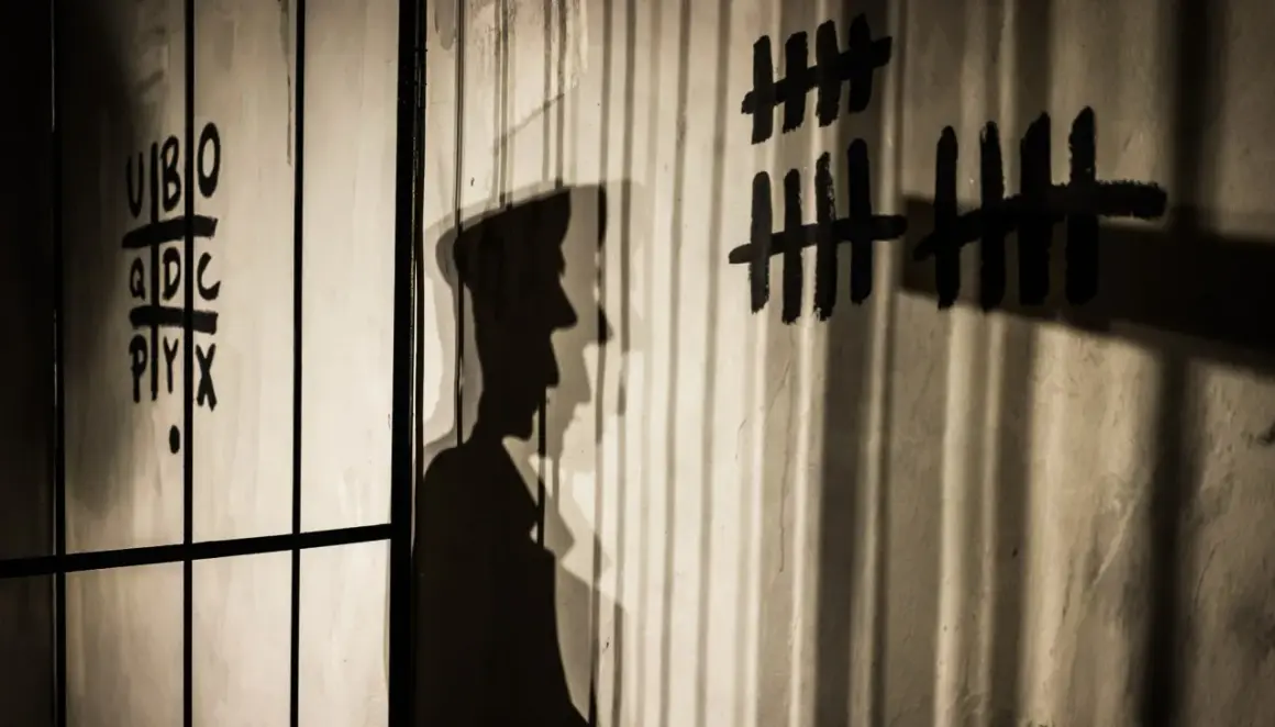 Shadows cast by bars and a figure on a wall with tally marks and letters. This image illustrates how to avoid shadows in indoor photography by using them creatively.