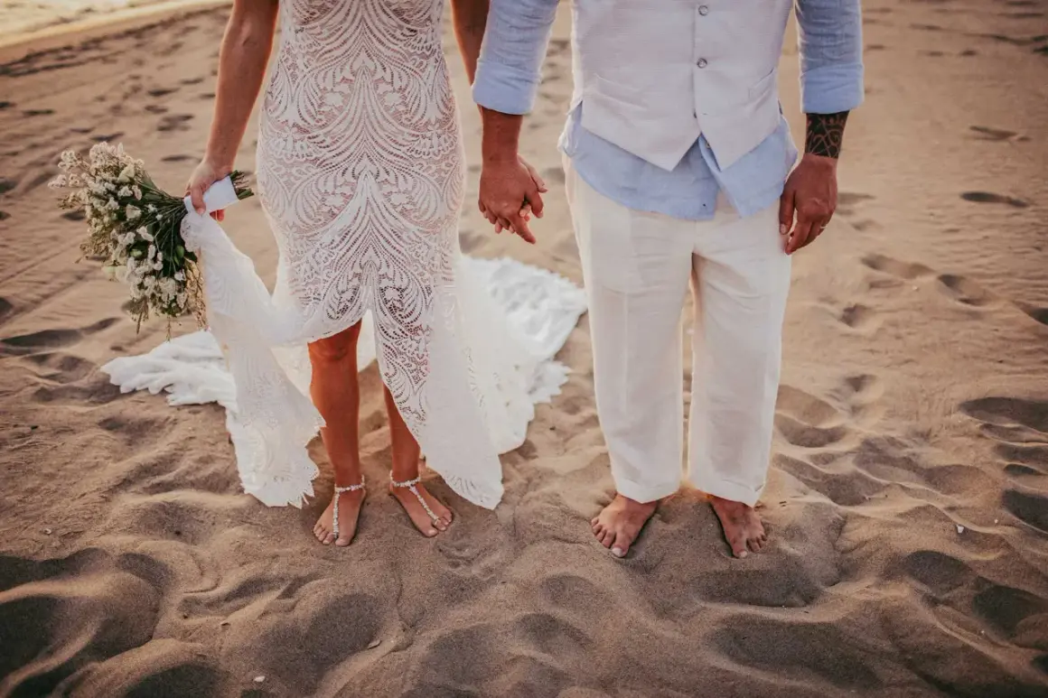 Coppia felice in un matrimonio spiaggia. La sposa con un bouquet, lo sposo con un gilet leggero.