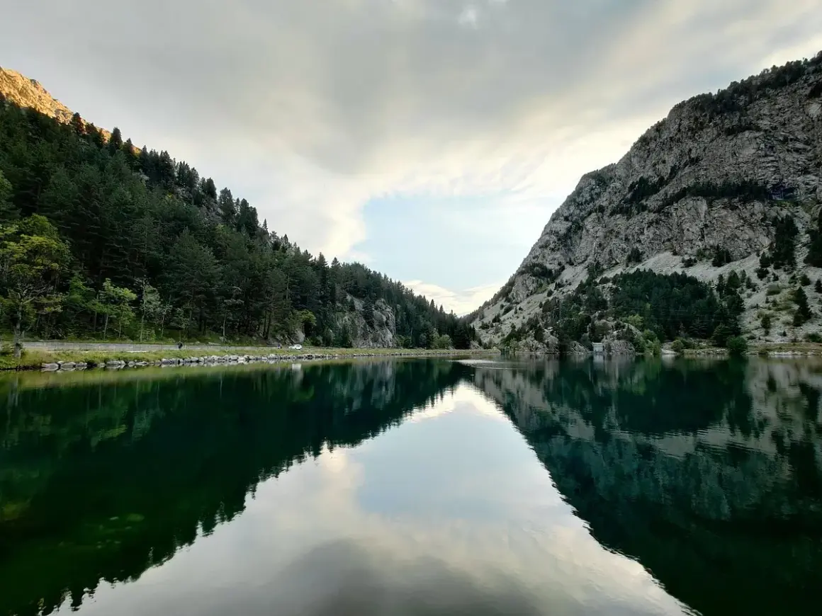 Reflejos perfectos en el ibon de Baños, rodeado de bosques y montañas rocosas. Un paisaje sereno y majestuoso.