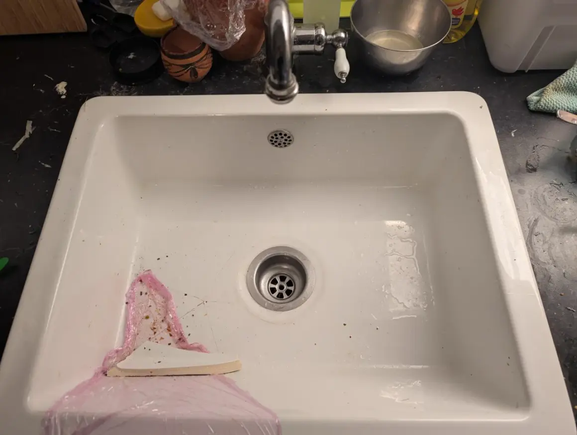 Un évier blanc avec un robinet chromé. Un outil blanc est utilisé pour aider à comment enlever un évier collé au silicone.