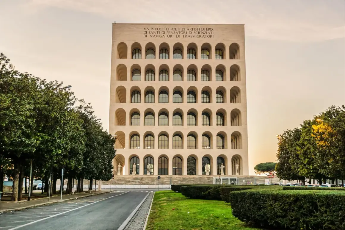 Il Colosseo Quadrato, imponente edificio con arcate sovrapposte, si erge maestoso tra alberi verdi e un cielo tenue.