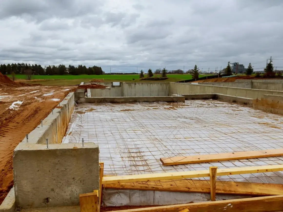 Fundament betonowy w budowie, z widocznymi zbrojeniem i folią. Trudno oszacować ile bloczków betonowych na fundament zużyto.