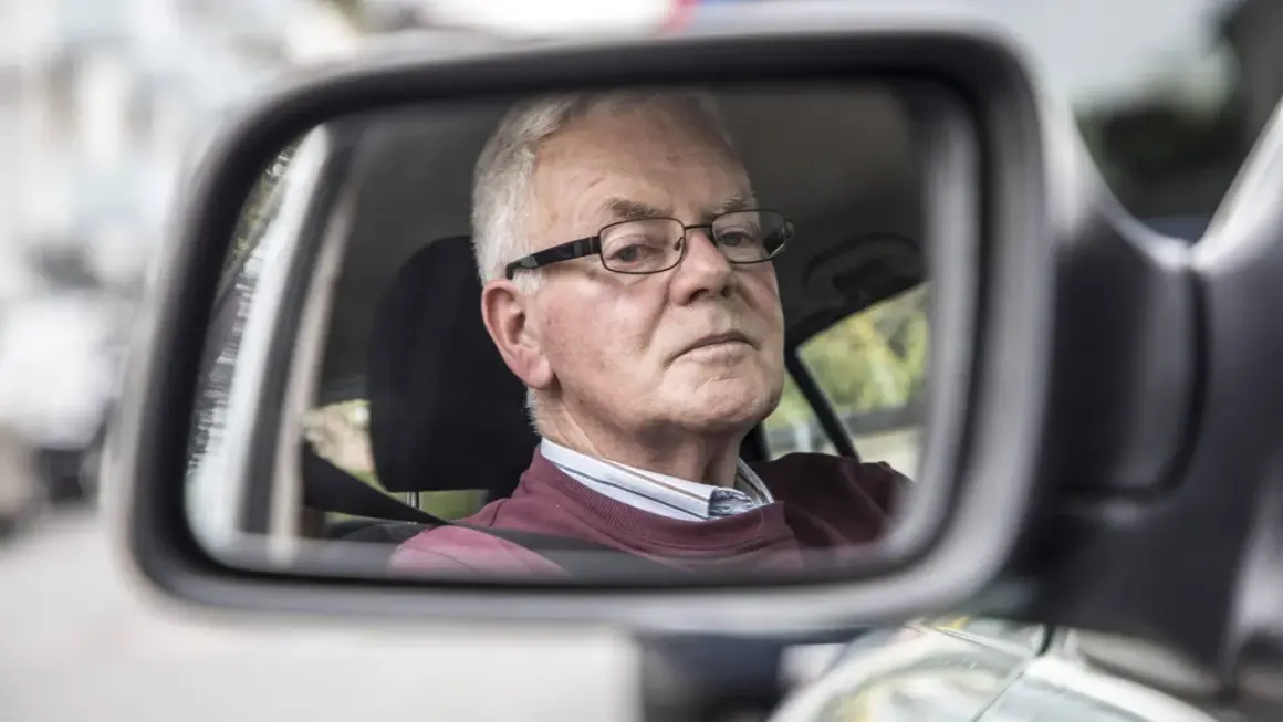 Älterer Mann mit Brille im Rückspiegel, der sich fragt, warum das Auto quietscht.