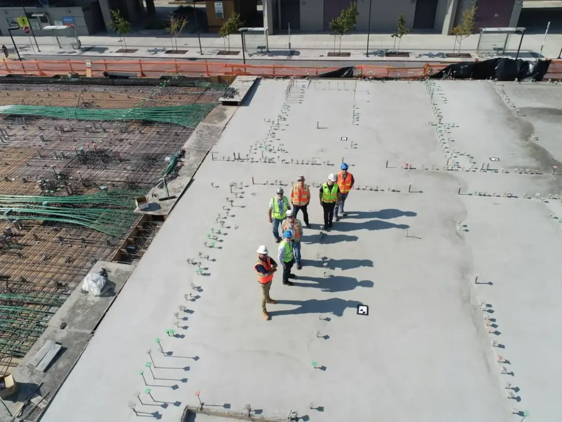 Grupa budowlańców na placu budowy. Zastanawiają się, ile kosztuje gruszka betonu, patrząc na zbrojenie i wylany fundament.