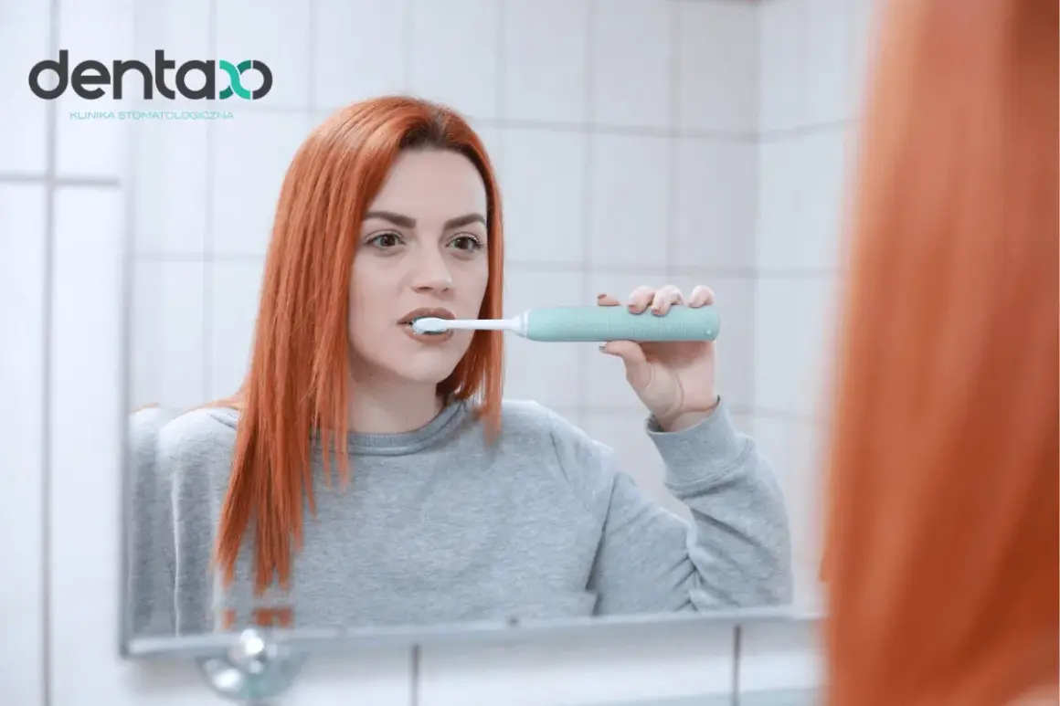 Ruda kobieta myje zęby elektryczną szczoteczką, zastanawiając się, ile razy dziennie myć zęby dla optymalnej higieny.