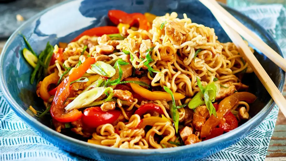 Schüssel mit Nudeln, Paprika, Frühlingszwiebeln und Hühnchen. Ein Teller mit einfachen asiatischen Gerichten, bereit zum Genießen mit Stäbchen.